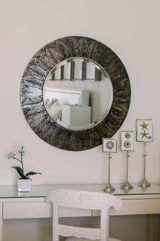 In this image, there's an elegant and well-decorated interior scene featuring a circular mirror with a decorative frame that has a leaf pattern
