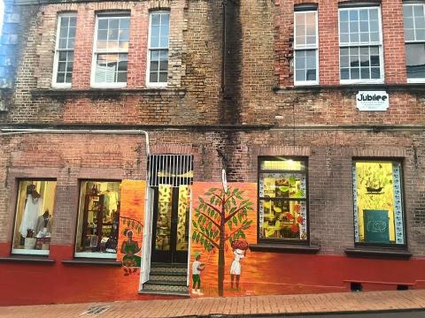 Rustic brick building with mural of two children and a tree, sign reads "Jubilee", shop windows display items.