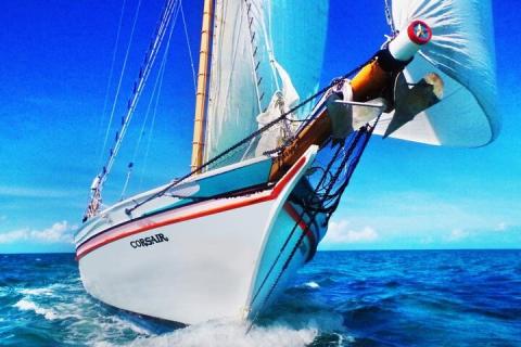 Close-up of sailboat "Corsair" cutting through water with unfurled sails under a clear blue sky.