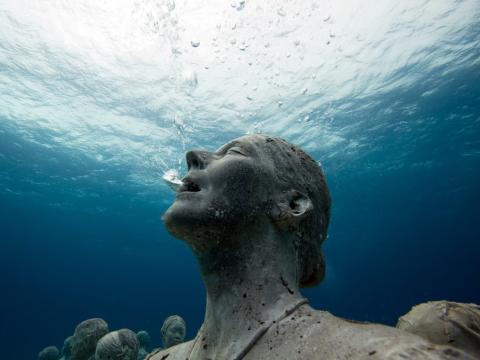 Underwater statue of a serene human figure with bubbles escaping from the mouth, light filtering down.