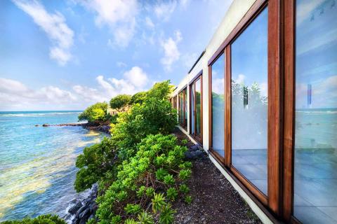 Modern coastal building with large windows and lush greenery by a calm sea