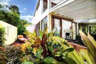 Modern house with large windows surrounded by lush tropical garden and outdoor seating