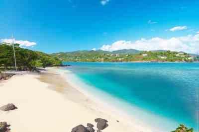 Secluded tropical beach with white sand, clear blue water, and green hills
