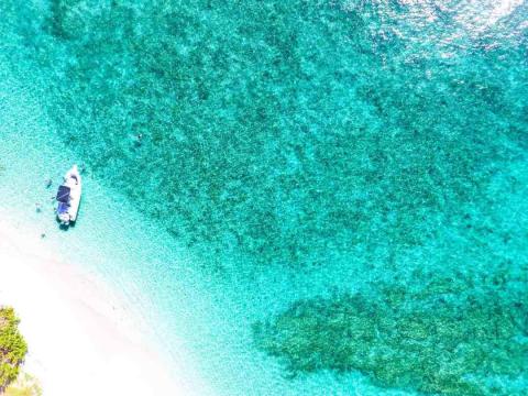 Aerial view of small boat by sandy shore in clear blue waters, ideal for tropical activities