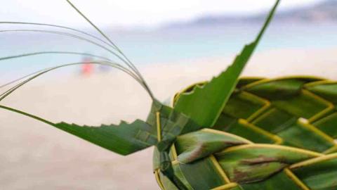 Green palm leaf woven basket on a blurry beach background