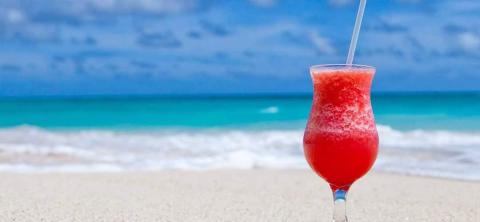 Refreshing red cocktail on sandy beach with clear turquoise waters in background