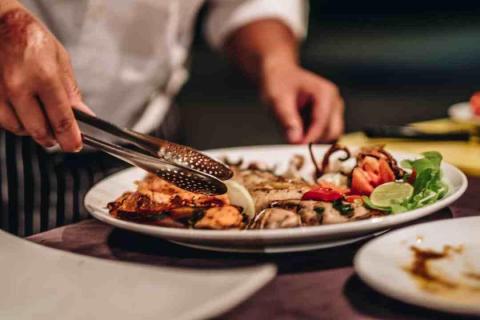 Chef plating seafood dish with octopus, lime, and chili in kitchen