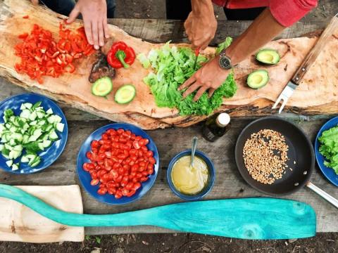Outdoor cooking scene with two people chopping vegetables and nuts