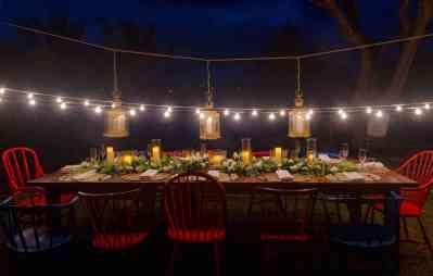 Outdoor dining setup at night with candles, foliage, colorful chairs, and string lights.