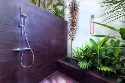 Modern outdoor shower with metallic head, stone floor, surrounded by lush greenery