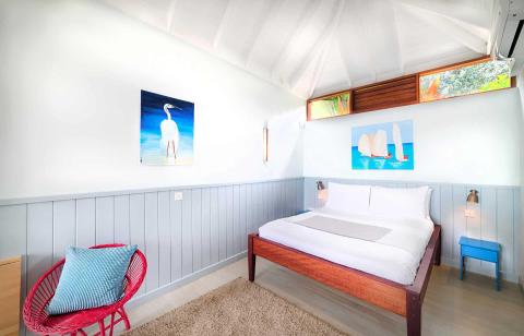Colorful bedroom with sloped ceiling, artwork, and tropical decor.