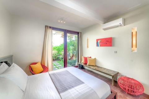 Cozy bedroom with a large bed, colorful nook, and garden view through glass door.