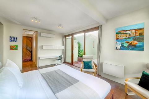 Modern bedroom with large bed, natural light, vibrant artwork, and sleek workspace.