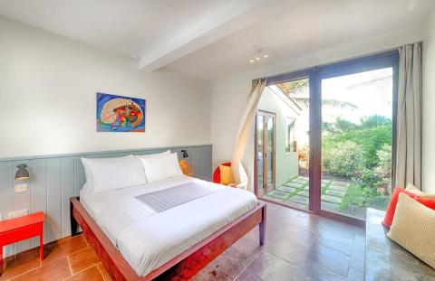 Cozy bedroom with large bed, abstract art, and garden view through glass doors.