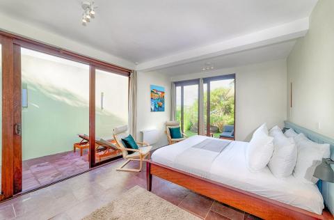 Modern bedroom with large bed, tile floors, and garden view through glass doors.