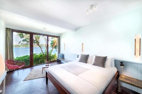 Modern bedroom with sea view, double bed, red chair, and balcony.