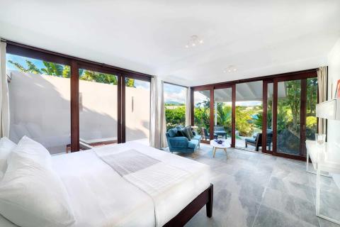Luxurious bedroom with white bed, blue sofa, large windows, and scenic view