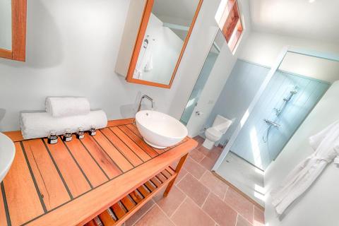 Modern bathroom with wooden bench, built-in sink, large mirror, and walk-in shower