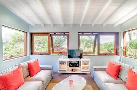 Modern living room with gray sofas, red-orange cushions, and tropical view.