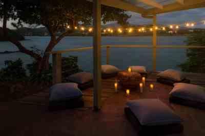 Cozy waterfront terrace with string lights and cushions at twilight.