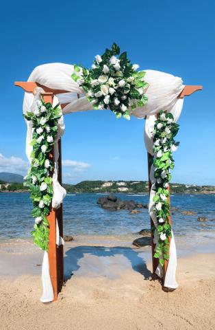 Romantic beach wedding arch with white flowers and fabric overlooking serene water