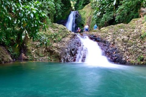 Multi-tiered waterfall in lush forest with a turquoise pool, rocks, and visitors climbing nearby.