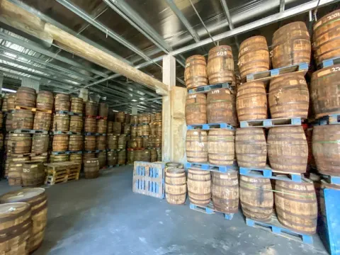 Efficient Barrel Storage in Distillery Warehouse Warehouse interior filled with neatly stacked wooden barrels on blue pallets for storage.