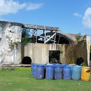 Abandoned Industrial Site with Weathered Barrels and Dilapidated Structures Old industrial building with blue and yellow barrels, peeling paint, and overgrown vegetation