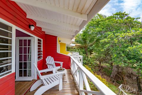 Red wooden house with white chair on porch overlooking lush greenery