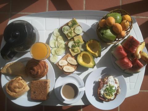 Colorful breakfast spread with fresh fruits, pastries, bacon, and eggs on a white table.