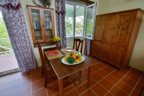 Cozy dining area with wooden table, fruit bowl, and lush outdoor view.