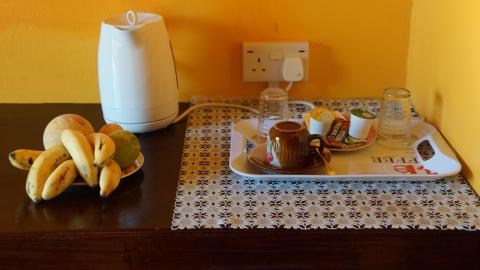 Hotel room serving table with fruit, electric kettle, and tea setup against a yellow wall.