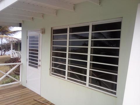 Light green coastal building with white trim, porch, and tropical backdrop