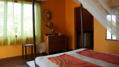 Bright orange bedroom with white mosquito net, wooden furniture, and colorful accents.