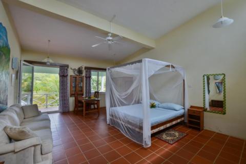 Tropical style bedroom with canopy bed, sectional sofa, and terracotta floors.