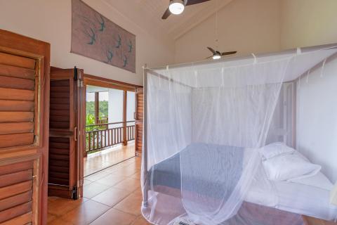 Tropical bedroom with mosquito net, balcony view, ceiling fan, and fish motif art