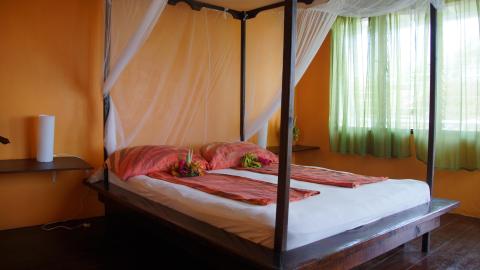 Colorful tropical bedroom with orange walls and four-poster bed, cozy and inviting.