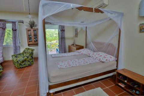 Cozy bedroom with wooden bed, floral bedspread, and lush greenery outside window.