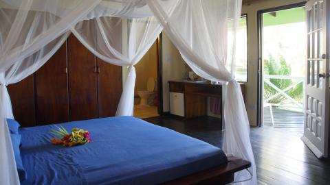Tropical resort bedroom with mosquito netting, floral decor, and open balcony view.