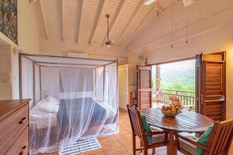 Tropical four-poster bed room with balcony overlooking lush hills