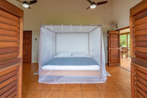 Tropical bedroom with white mosquito net, wooden panels, and a view of lush greenery