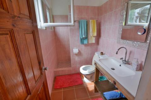 Small pink-toned bathroom with white fixtures, wooden vanity, and colorful towels.