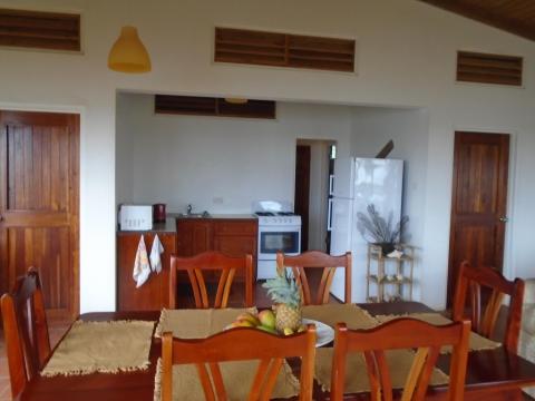 Rustic dining room with wooden table, chairs, and kitchen area.