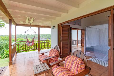 Covered patio with hammock, chairs, and view of greenery and water, tropical resort setting.