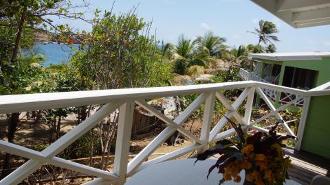 Scenic tropical beach view from a balcony with lush greenery and calm blue sea.