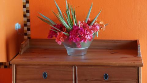 Wooden dresser with silver bowl of flowers against an orange wall, decorative and tidy.