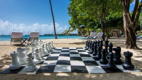 Outdoor large chess set on a sandy beach with sea view and lounge chairs
