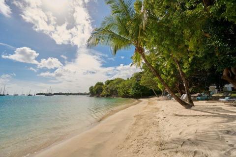 Tranquil beach with sun loungers and boats under partly cloudy skies.