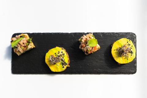 Gourmet appetizers on slate board with mango slices and salad-topped crackers