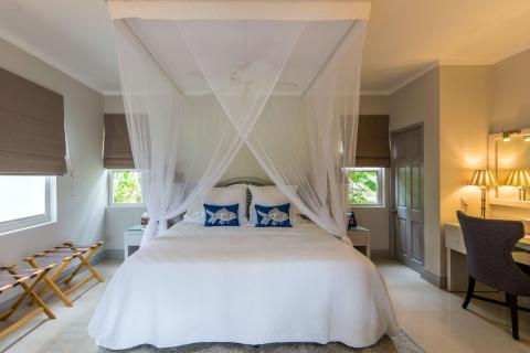 Elegant tropical bedroom with a white mosquito-netted double bed and wooden decor